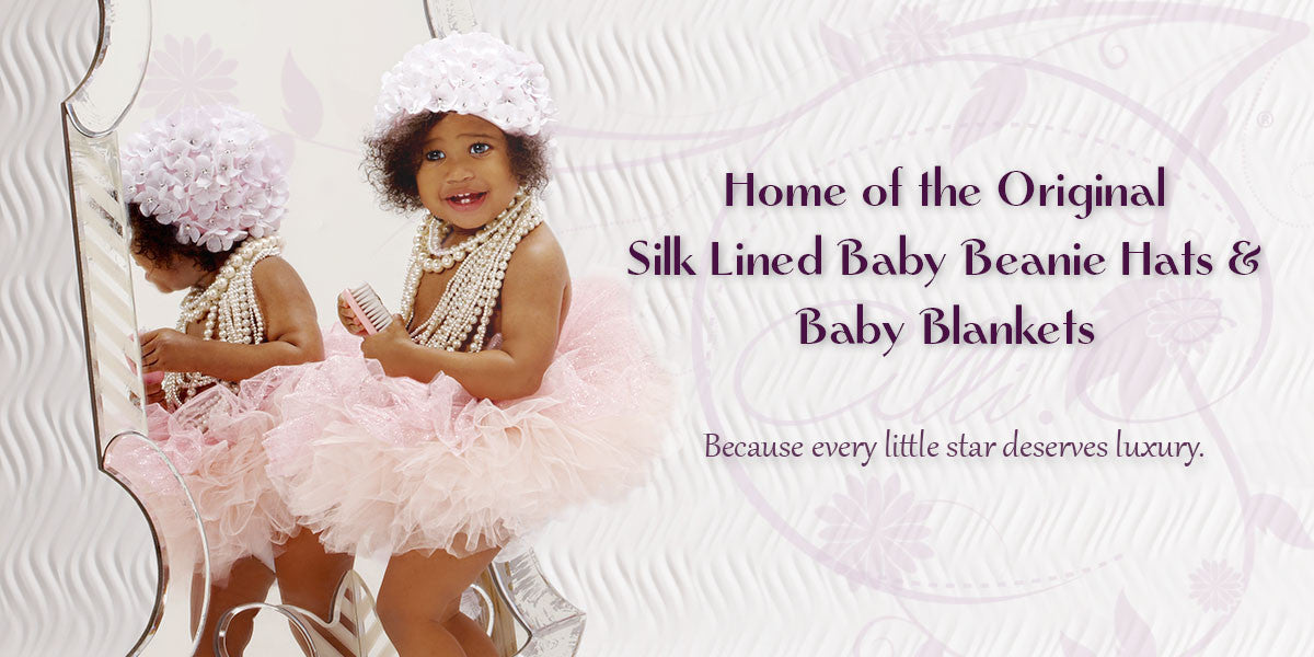 Toddler girl in tutu looking in mirror wearing an Alli.C pink beanie hat that has white flowers all over with Swarovski crystal centers. The Alli.C beanie hat has a white silk lining. Text on side of toddler girl reads home of the original silk-lined baby beanie hats and baby blankets, because every little star deserves luxury.