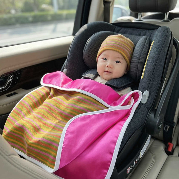 Baby girl in a car seat wearing Alli.C colorful striped beanie hat & matching baby blanket with silk lining inside a vehicle.
